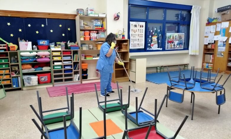 Mujer limpiando aula de guardería con mesas volteadas.