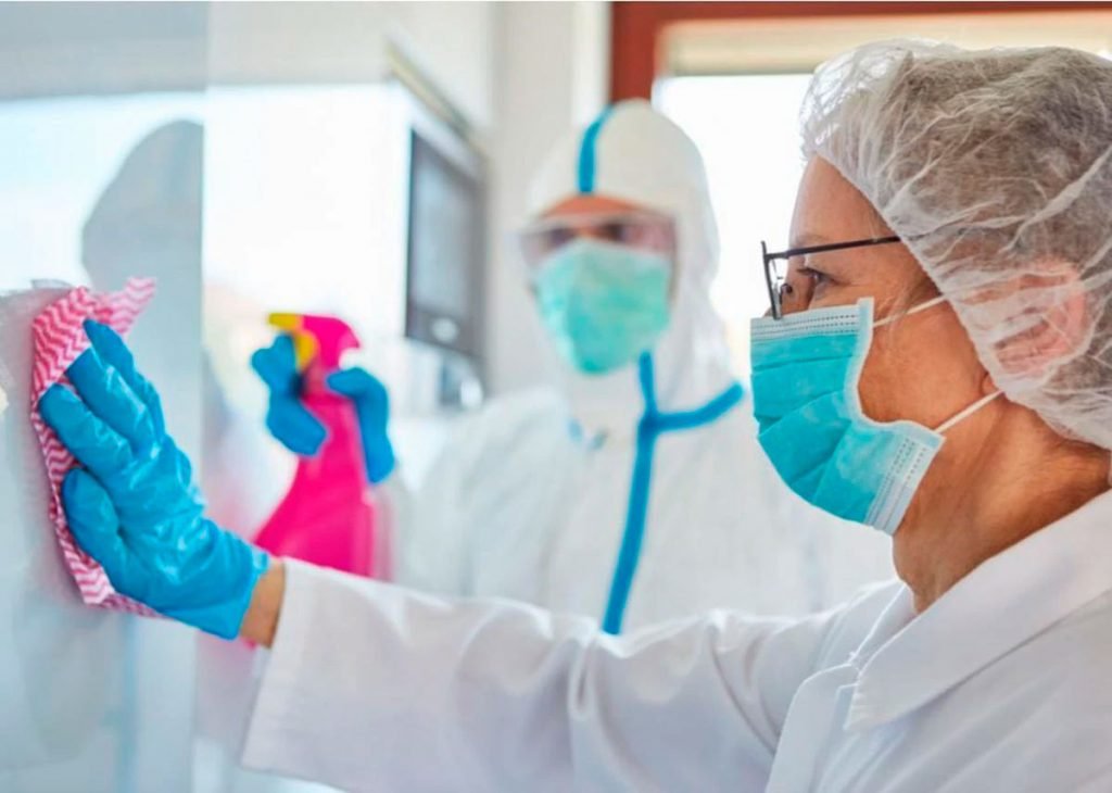 Personal médico limpiando superficie con trajes protectores.