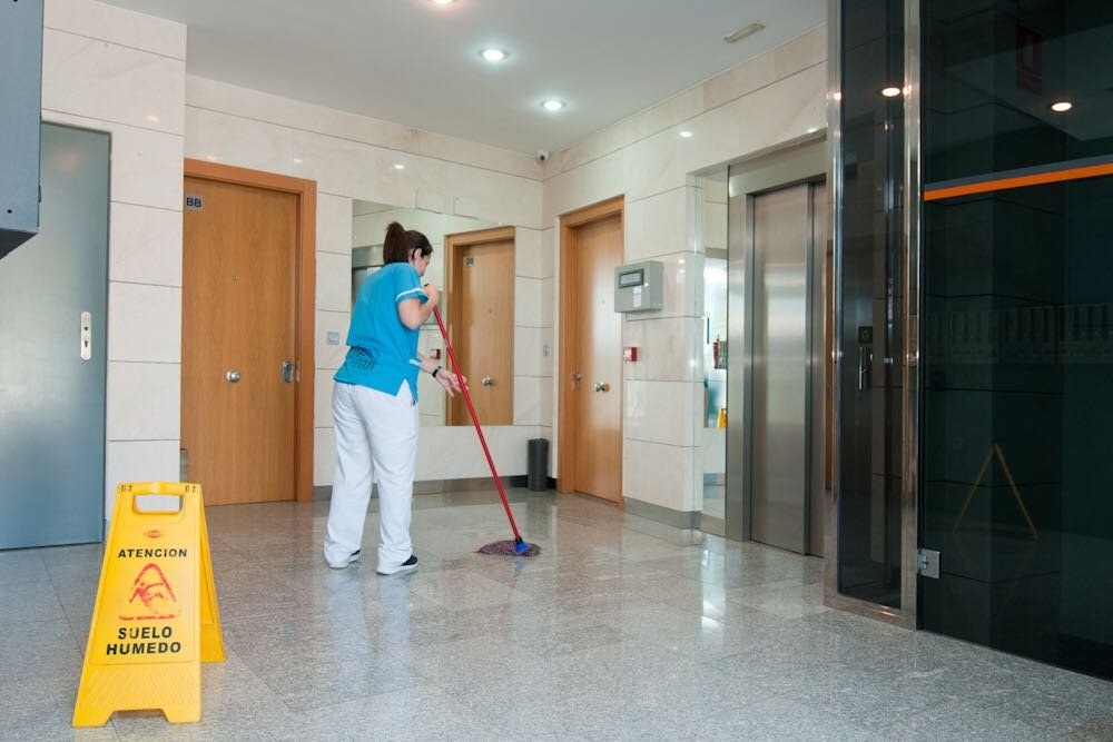 Personal de limpieza fregando en edificio, suelo mojado.