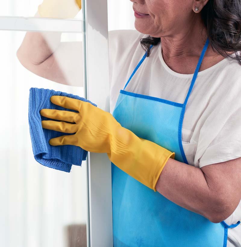 Mujer limpiando ventana con guantes amarillos
